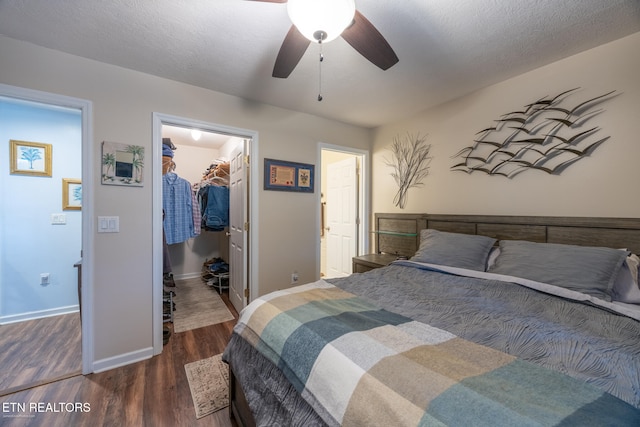 bedroom featuring a textured ceiling, ceiling fan, dark wood-type flooring, a spacious closet, and a closet