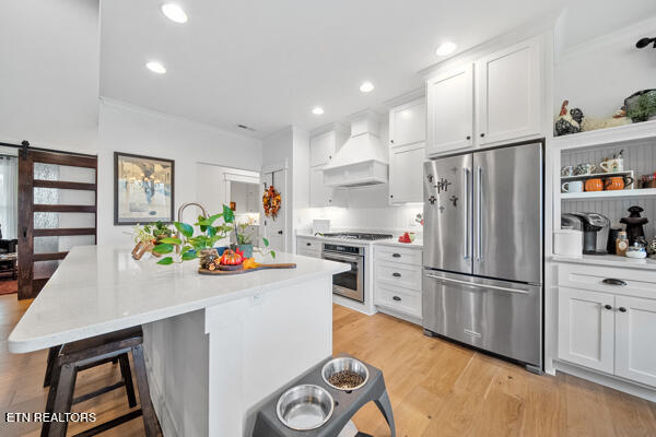 kitchen with custom range hood, a barn door, stainless steel appliances, and white cabinetry