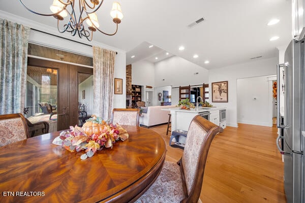 dining space with sink, an inviting chandelier, crown molding, light hardwood / wood-style floors, and vaulted ceiling