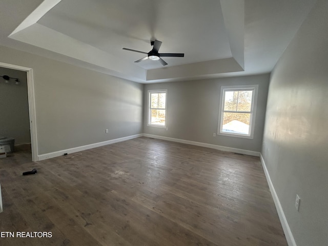 empty room with dark wood-type flooring, ceiling fan, and a raised ceiling