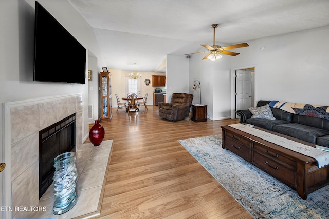 living room featuring ceiling fan with notable chandelier, a tile fireplace, and light hardwood / wood-style flooring