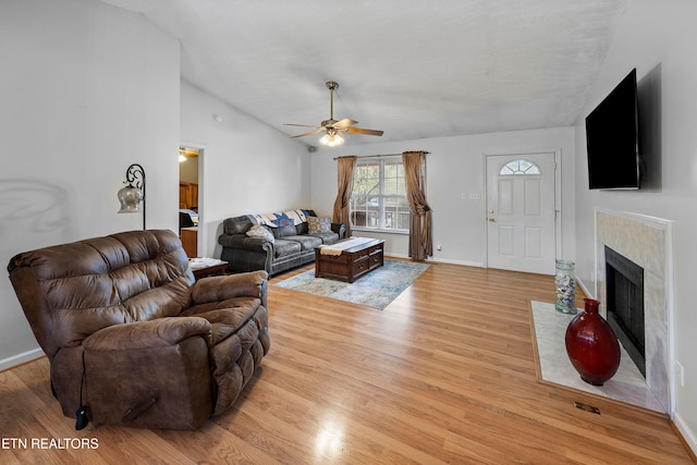 living room with ceiling fan, light wood-type flooring, a premium fireplace, and vaulted ceiling