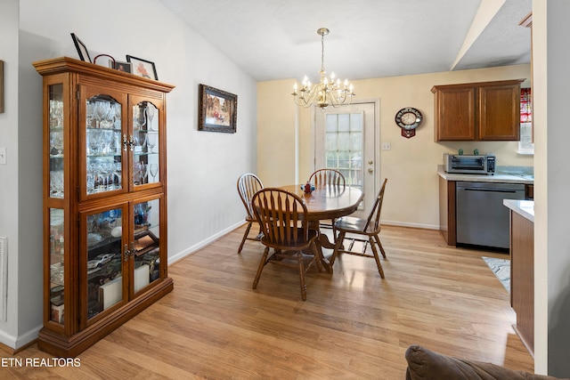 dining space featuring an inviting chandelier, vaulted ceiling, and light hardwood / wood-style flooring