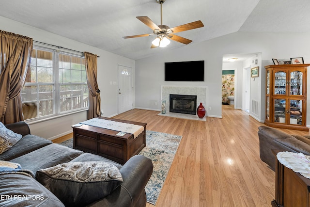 living room with ceiling fan, a fireplace, lofted ceiling, and light wood-type flooring