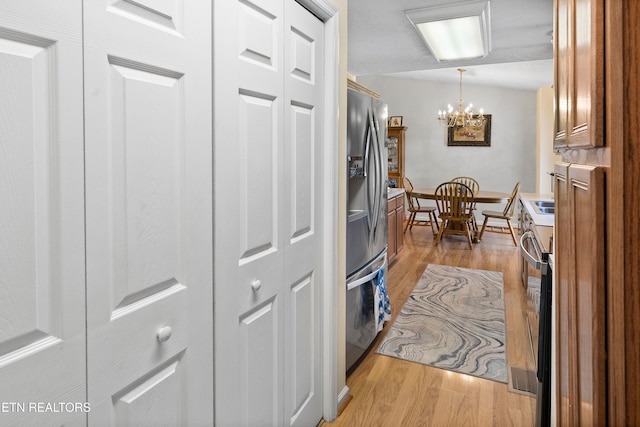 kitchen with a chandelier, hanging light fixtures, stainless steel appliances, and light hardwood / wood-style floors