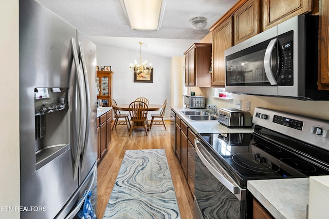 kitchen with appliances with stainless steel finishes, vaulted ceiling, a notable chandelier, light hardwood / wood-style floors, and hanging light fixtures