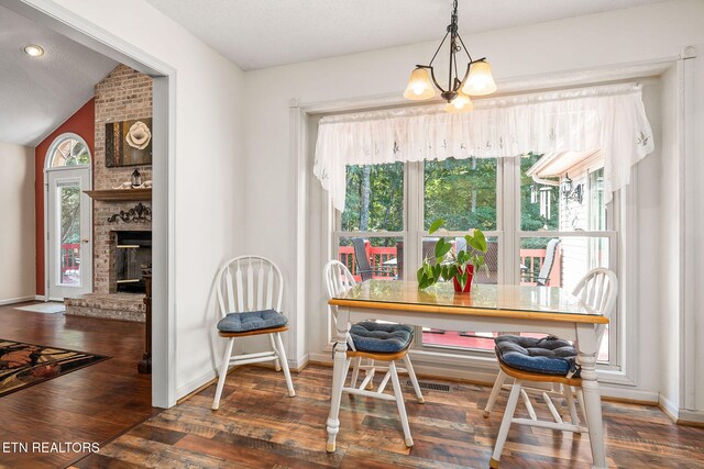 dining space featuring a notable chandelier, dark hardwood / wood-style floors, lofted ceiling, and a brick fireplace