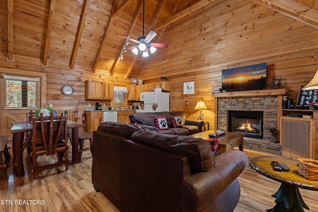 living room with a stone fireplace, wooden walls, ceiling fan, light wood-type flooring, and beamed ceiling