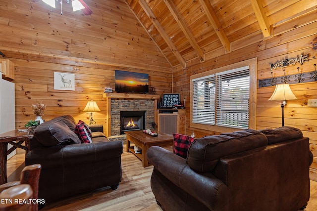 living room featuring light wood-type flooring, wooden walls, high vaulted ceiling, beamed ceiling, and a stone fireplace