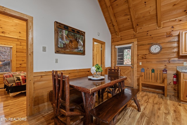 dining room with beamed ceiling, high vaulted ceiling, wooden walls, wood ceiling, and light wood-type flooring