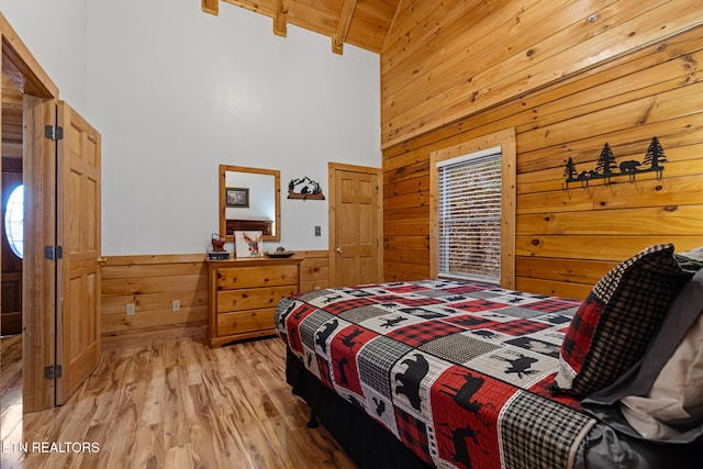 bedroom with beamed ceiling, wood walls, light wood-type flooring, and high vaulted ceiling