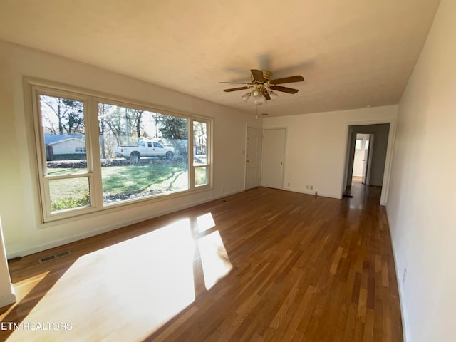 spare room with dark wood-type flooring, ceiling fan, and a healthy amount of sunlight