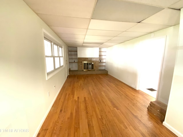 unfurnished living room featuring a brick fireplace, a paneled ceiling, and light hardwood / wood-style flooring