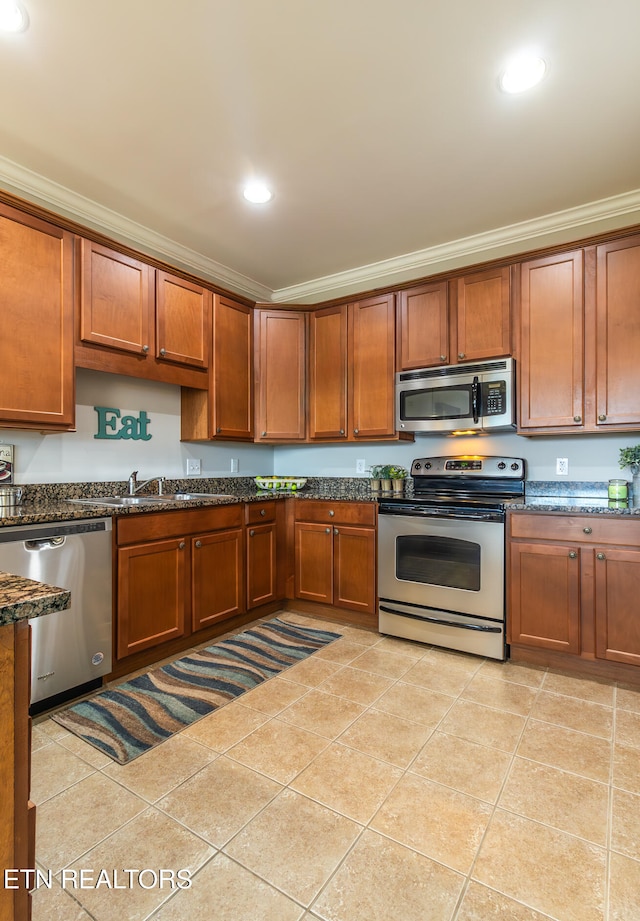 kitchen with dark stone countertops, crown molding, light tile patterned floors, and stainless steel appliances