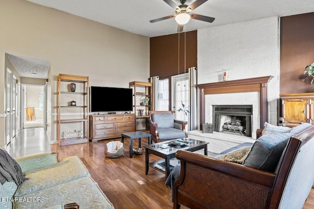 living room with hardwood / wood-style floors, ceiling fan, a towering ceiling, a fireplace, and a textured ceiling