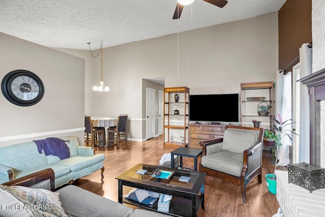 living room featuring ceiling fan with notable chandelier, hardwood / wood-style floors, a textured ceiling, and a towering ceiling