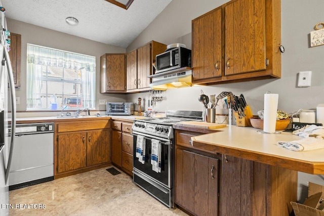 kitchen featuring kitchen peninsula, appliances with stainless steel finishes, a textured ceiling, vaulted ceiling, and sink