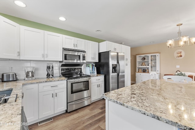 kitchen with white cabinetry, light wood-type flooring, decorative light fixtures, and appliances with stainless steel finishes