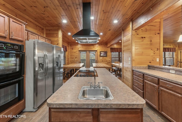 kitchen with island exhaust hood, wooden walls, a center island with sink, and black appliances