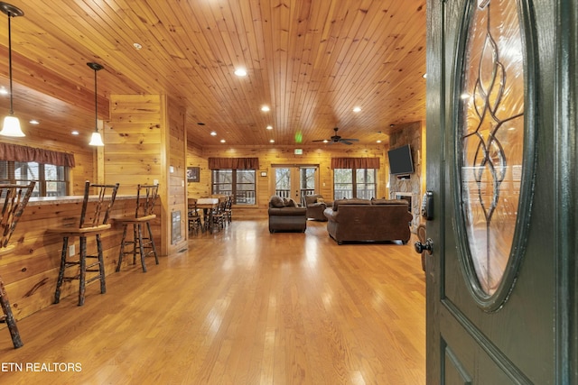 foyer with wood ceiling, ceiling fan, light wood-type flooring, and wooden walls