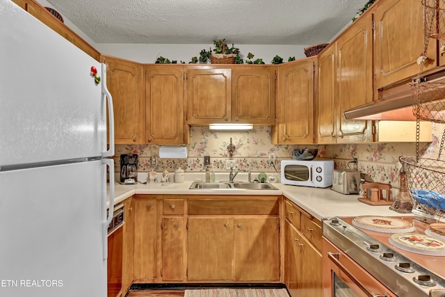 kitchen with a textured ceiling, white appliances, and sink