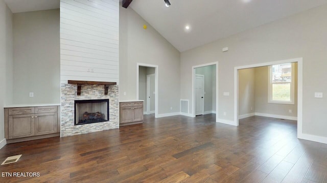 unfurnished living room featuring a stone fireplace, baseboards, visible vents, and dark wood finished floors