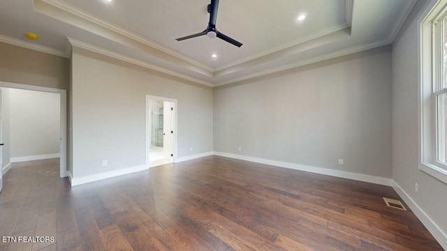 spare room with a ceiling fan, dark wood finished floors, a tray ceiling, and visible vents