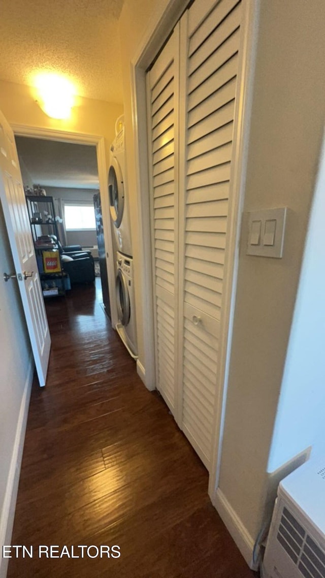 corridor featuring a textured ceiling, dark hardwood / wood-style flooring, and stacked washer and dryer