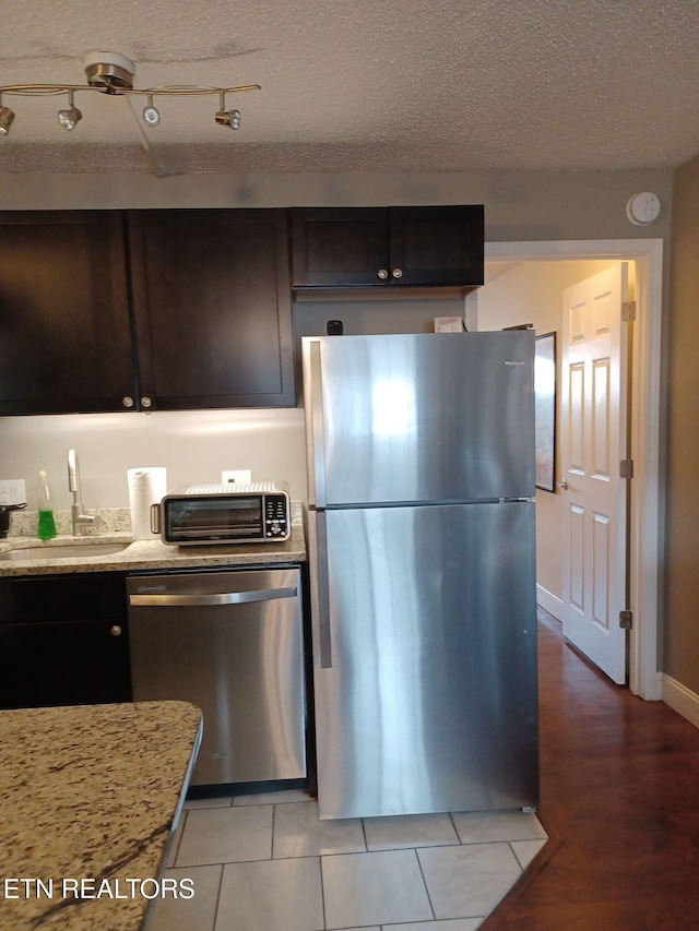 kitchen featuring light stone countertops, appliances with stainless steel finishes, a textured ceiling, sink, and light hardwood / wood-style floors