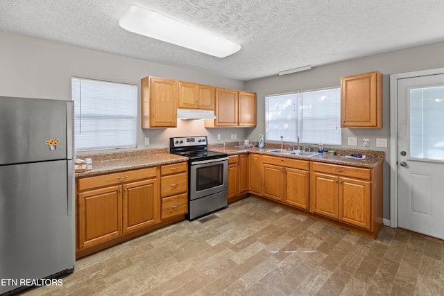 kitchen with light stone countertops, sink, stainless steel appliances, a textured ceiling, and light wood-type flooring