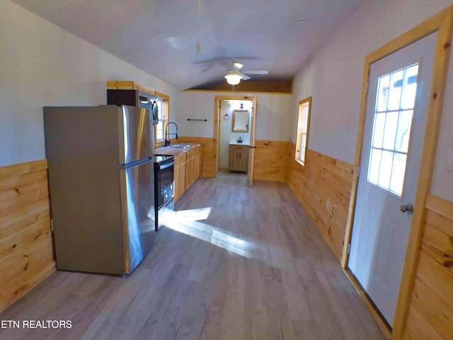 kitchen featuring wooden walls, ceiling fan, stainless steel fridge, light wood-type flooring, and light brown cabinetry