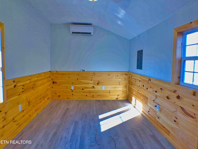 unfurnished room featuring an AC wall unit, wooden walls, wood-type flooring, and vaulted ceiling