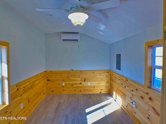 unfurnished room with vaulted ceiling, ceiling fan, hardwood / wood-style flooring, an AC wall unit, and wood walls