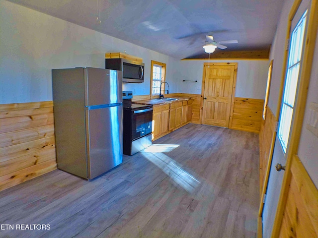 kitchen featuring ceiling fan, light hardwood / wood-style floors, wooden walls, light brown cabinetry, and appliances with stainless steel finishes