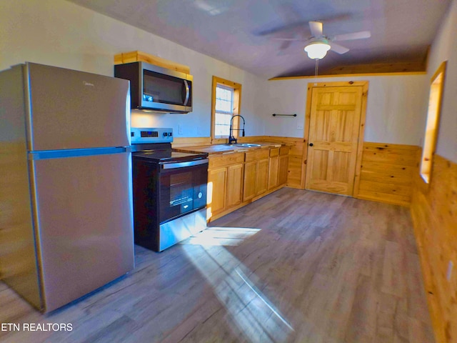 kitchen featuring appliances with stainless steel finishes, ceiling fan, sink, light hardwood / wood-style floors, and wood walls