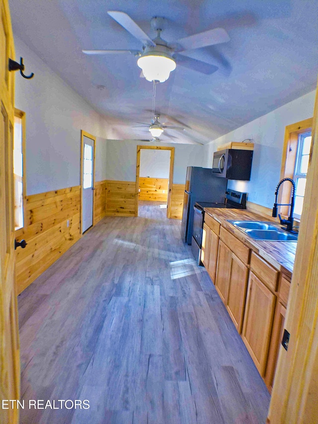 kitchen with sink, stainless steel appliances, dark hardwood / wood-style floors, lofted ceiling, and wooden walls