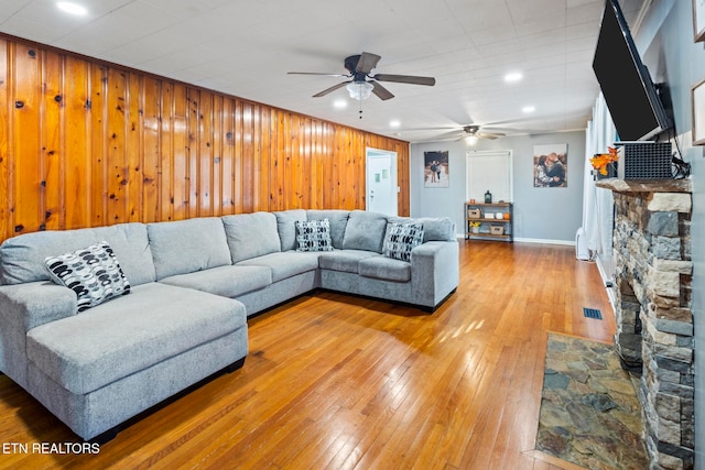 living room featuring hardwood / wood-style flooring, ceiling fan, a fireplace, and wooden walls