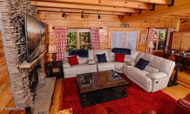 living room with beamed ceiling, wood walls, a stone fireplace, and hardwood / wood-style flooring