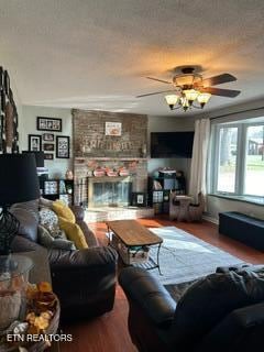 living room featuring a fireplace, wood-type flooring, a textured ceiling, and ceiling fan