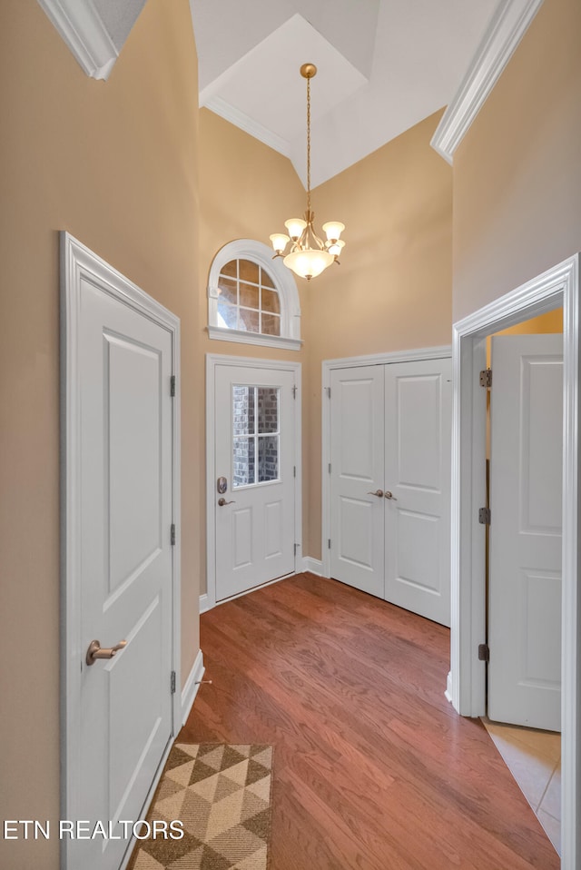 entrance foyer with crown molding, a towering ceiling, light hardwood / wood-style floors, and a notable chandelier