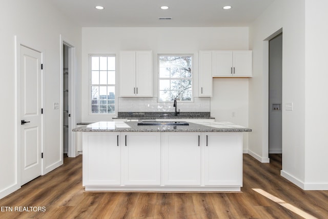 kitchen with light stone counters, dark hardwood / wood-style flooring, white cabinets, and a kitchen island