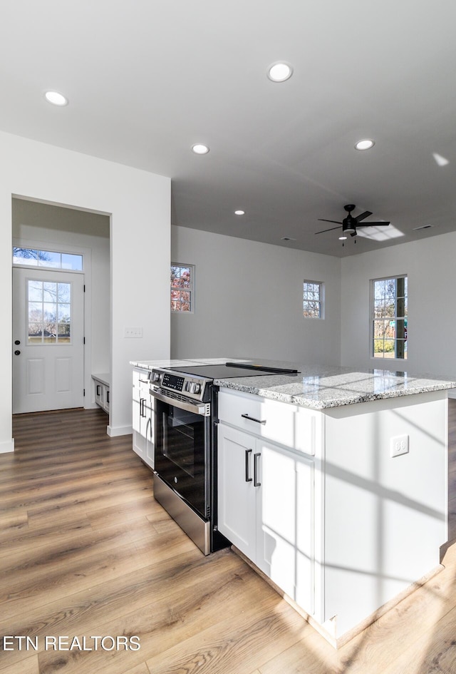 kitchen featuring stainless steel range with electric stovetop, white cabinets, ceiling fan, light stone countertops, and light hardwood / wood-style floors