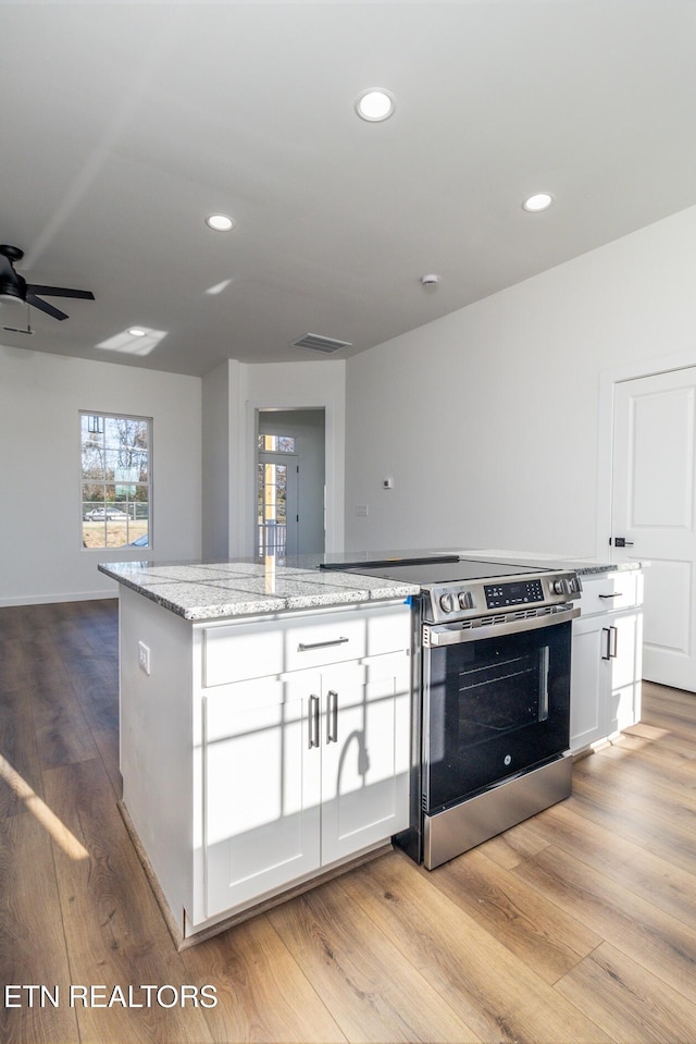 kitchen featuring light hardwood / wood-style floors, stainless steel range oven, white cabinetry, and a kitchen island