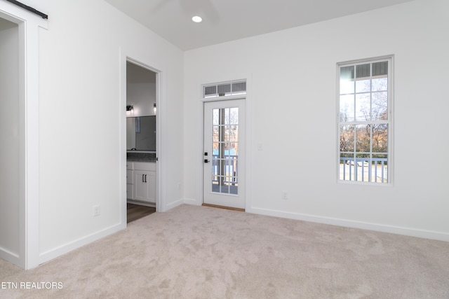 unfurnished room with a barn door and light colored carpet