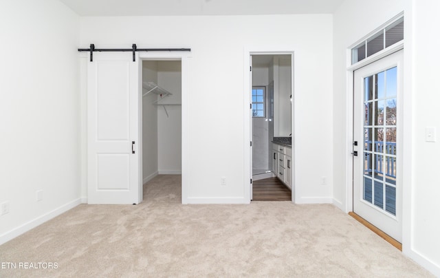 unfurnished bedroom featuring a spacious closet, a barn door, ensuite bathroom, light carpet, and a closet