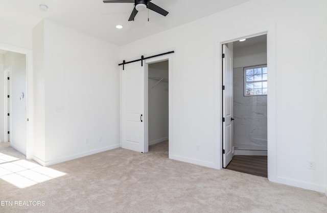 unfurnished bedroom featuring ceiling fan, a barn door, ensuite bathroom, a walk in closet, and a closet