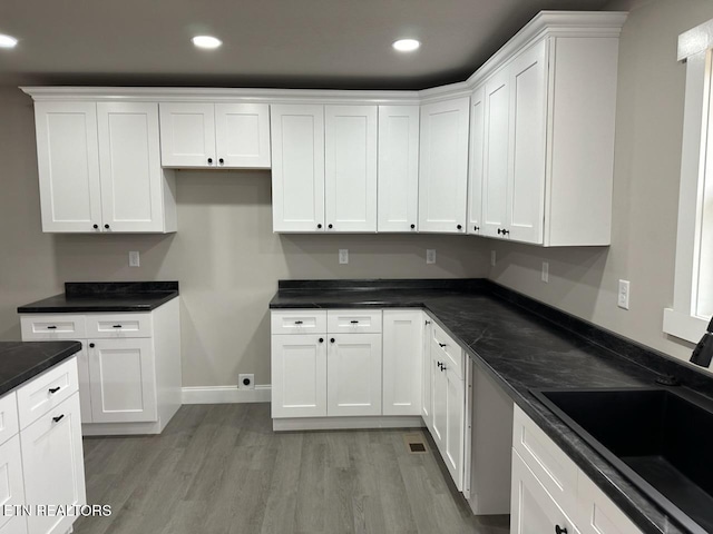 kitchen featuring sink, white cabinets, dark stone counters, and light hardwood / wood-style flooring