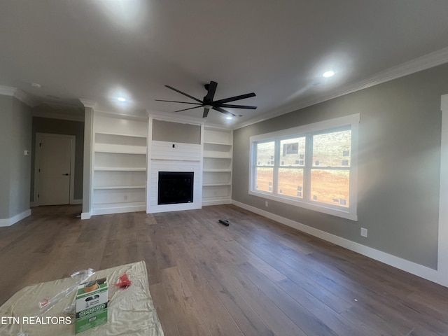 unfurnished living room featuring ceiling fan, a fireplace, wood finished floors, baseboards, and crown molding