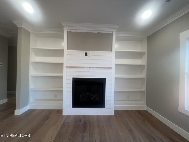 unfurnished living room with crown molding, built in shelves, dark wood-style flooring, and baseboards