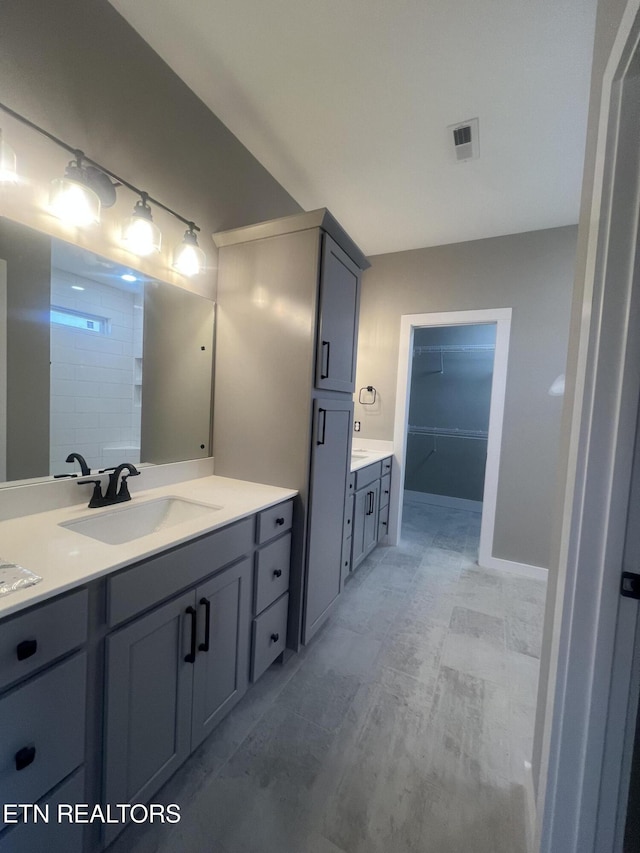 full bath with vanity, a walk in closet, visible vents, and baseboards